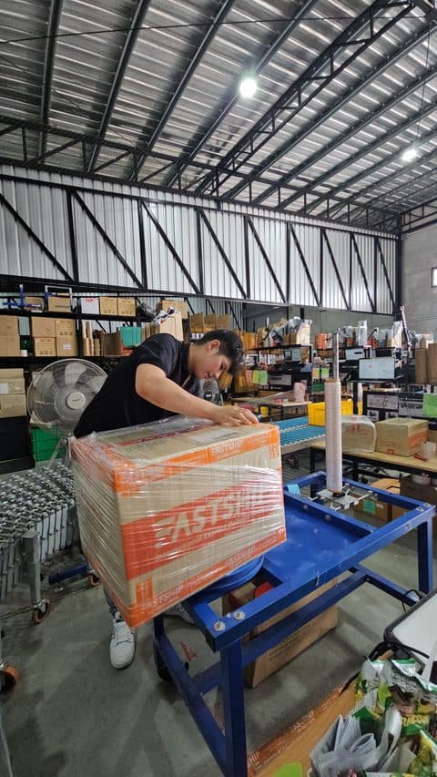 เจ้าหน้าที่ FastShip ห่อพลาสติกยืดหุ้มกล่องพัสดุก่อนส่งออก